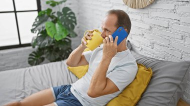 İspanyol orta yaşlı bir adam rahat yatak odasında rahat rahat pijamalarını giyiyor, sabah kahvesini yudumlarken akıllı telefonuyla ciddi bir konuşma yapıyor..