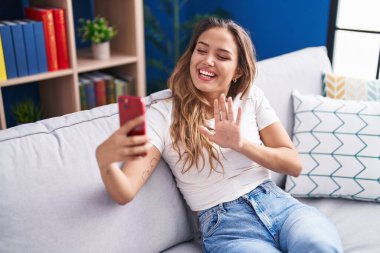 Genç İspanyol kadın akıllı telefonuyla görüntülü arama yapıyor. Pozitif ve mutlu görünüyor. Kendine güvenen bir gülümsemeyle dişlerini gösteriyor. 