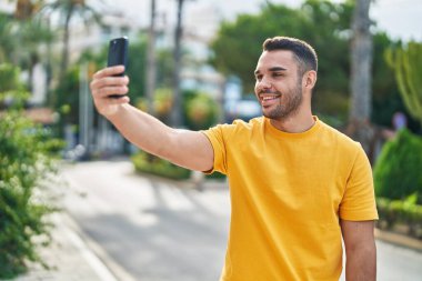 Genç İspanyol adam gülümsüyor. Parktaki akıllı telefonun yanında özçekim yapıyor.