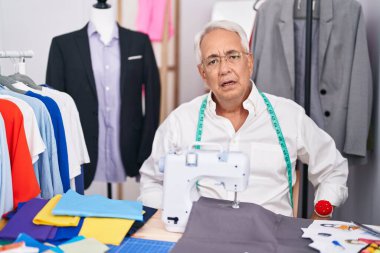 Orta yaşlı, gri kuaförlü, dikiş makinesi kullanan, ağzı açık, şüpheci ve alaycı görünen orta yaşlı bir adam. 