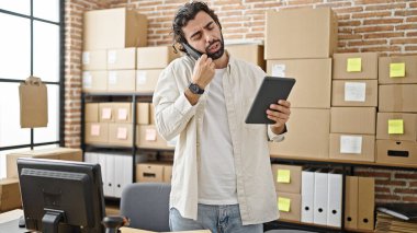 Latin kökenli genç bir iş adamı ofisteki telefonda konuşurken touchpad kullanıyor.