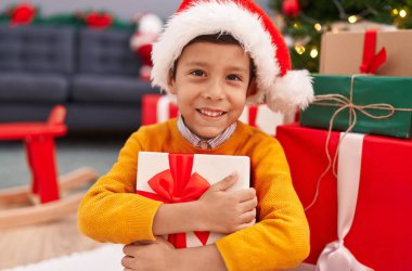Sevimli İspanyol çocuk Noel hediyesini kucaklıyor. Evde yerde oturuyor.