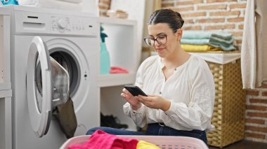 Çamaşır odasında akıllı telefon kullanan güzel İspanyol bir kadın.