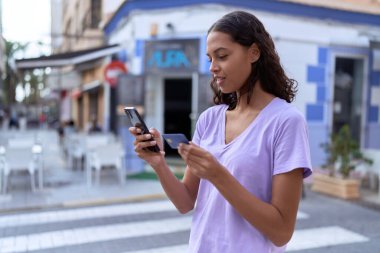 Young african american woman using smartphone and credit card at coffee shop terrace