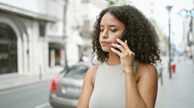 Genç ve güzel İspanyol bir kadın akıllı telefonda konuşuyor. Sokakta ciddi bir ifadeyle.