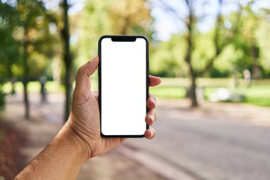Akıllı telefonu tutan adam parkta beyaz ekranı gösteriyor.