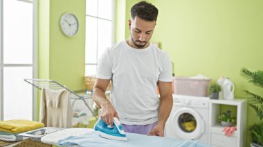 Young arab man ironing clothes at laundry room