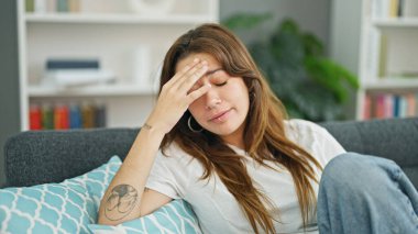 Young beautiful hispanic woman sitting on sofa with serious expression at home