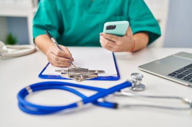 Genç, güzel İspanyol kadın doktor, klinikteki belgelerde akıllı telefon yazısını kullanıyor.