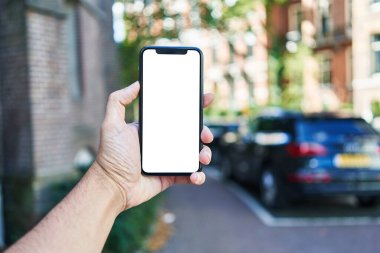 Akıllı telefon tutan adam araba parkında beyaz boş ekran gösteriyor.
