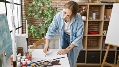 Sanat stüdyosunda duran genç kadın ressam kağıt üzerine resim çiziyor.
