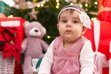 Sevimli İspanyol bebek evde Noel ağacının yanında yerde oturuyor.