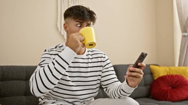 Sersemledim! Genç İspanyol 'un evde oturup akıllı telefon kullanırken, kahvesini yudumlarken yüzündeki şaşkınlık ifadesi.