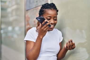 Afro-Amerikalı kadın gülümsüyor. Akıllı telefondan konuşuyor.