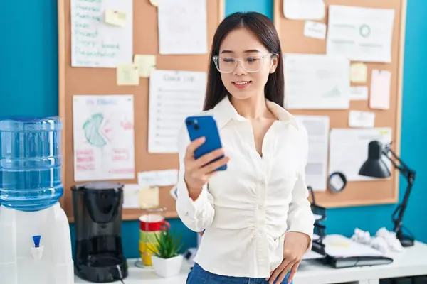 Young chinese woman business worker smiling confident using smartphone at office