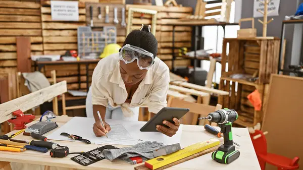 Attractive african american woman carpenter taking notes on touchpad at carpentry workshop