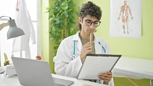 Young Hispanic Man Doctor Writing Medical Report Thinking Clinic — Stock Photo, Image