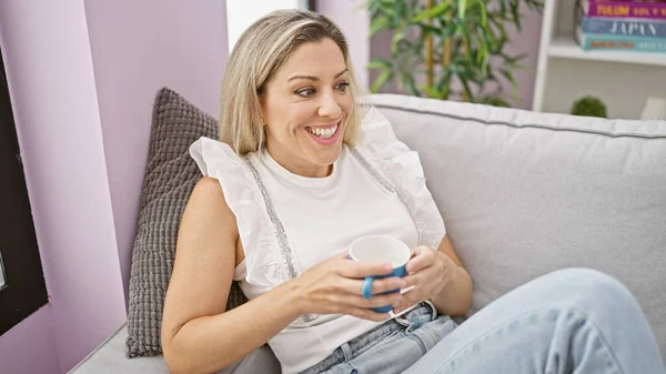Young Blonde Woman Drinking Coffee Sitting Sofa Home — Fotografia de Stock