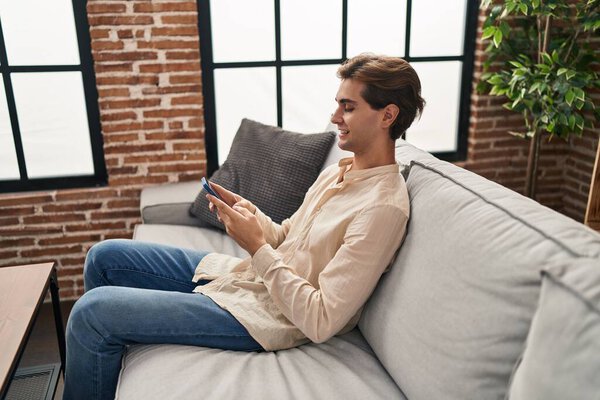Young caucasian man using smartphone sitting on sofa at home