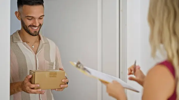 Young hispanic man receiving package signing on clipboard at street