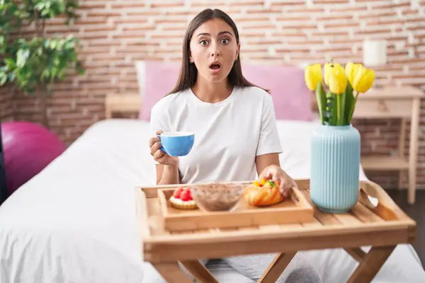 年轻的惊慌失措的女人吃着糕点当早餐坐在床上害怕 惊讶的表情 恐惧和兴奋的脸 — 图库照片