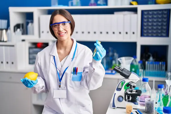 Young beautiful hispanic woman scientist holding lemon and test tube at laboratory