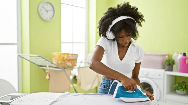 African american woman listening to music ironing clothes at laundry room