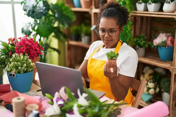 African american woman florist using laptop holding plant at flower shop