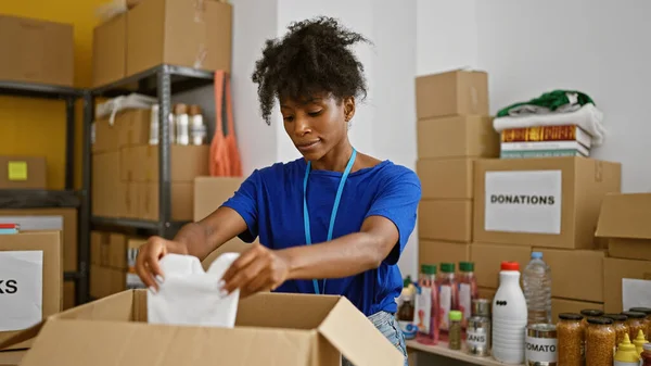 African american woman volunteer packing clothes on package at charity center