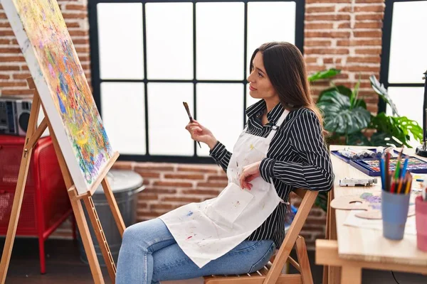 Young beautiful hispanic woman artist looking draw with serious expression at art studio