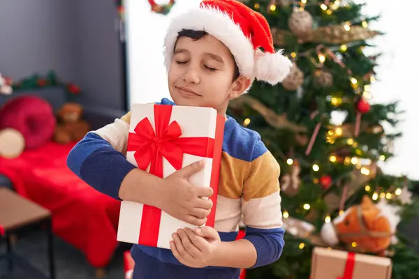 Adorable Hispanic Boy Hugging Christmas Gift Standing Home — Stock Photo, Image