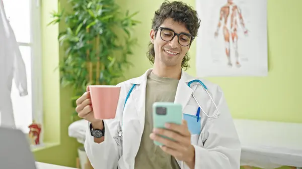 Joven Médico Hispano Usando Smartphone Bebiendo Café Clínica — Foto de Stock