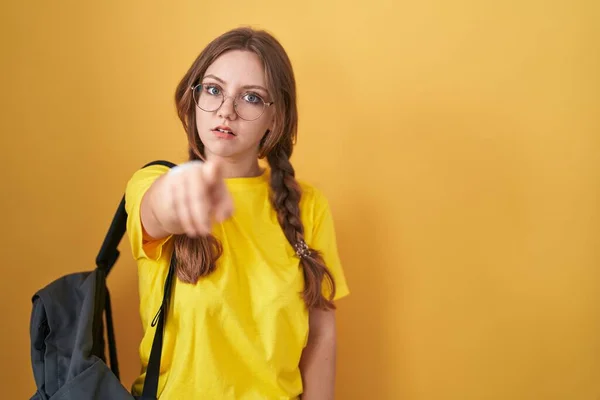 年轻的高加索女人背着学生背包 背着黄色的背景 带着不满和沮丧的目光看着摄像机 对你怒气冲冲 — 图库照片
