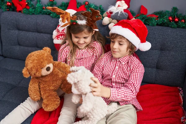 哥哥姐姐和泰迪熊在家里的圣诞装饰品旁坐在沙发上玩耍 — 图库照片
