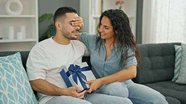 Man and woman couple surprised with gift covering eyes with hand at home
