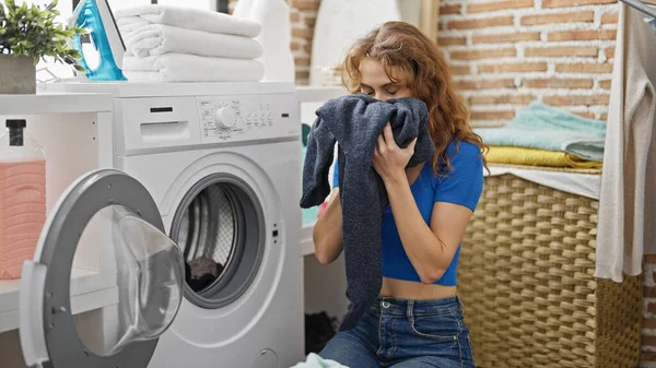 Young woman smelling clothes at laundry room