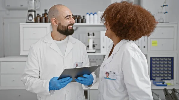 stock image Two smiling scientists in the lab, engrossed in a lively chat while scrutinizing documents on clipboard