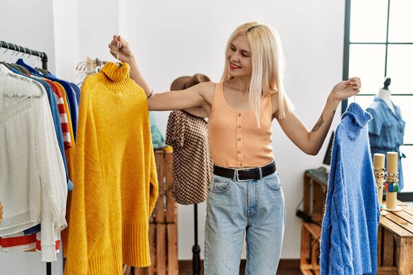 Young blonde woman customer choosing sweater smiling at clothing store