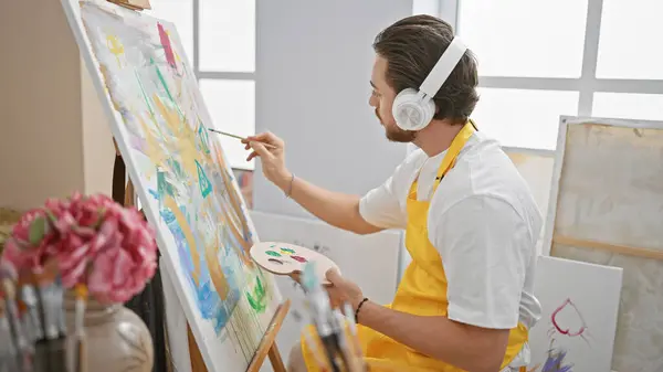 Young hispanic man artist listening to music drawing concentrated at art studio