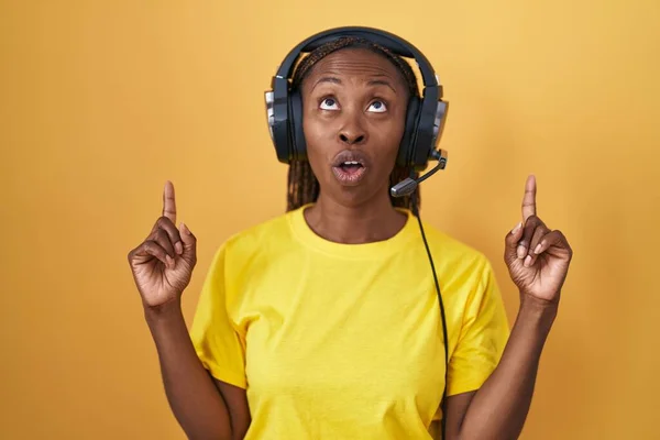非洲裔美国妇女使用耳机听音乐 惊讶地抬起头 用手指和胳膊指着音乐 — 图库照片