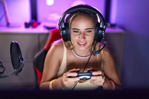 Young blonde woman streamer playing video game using joystick at gaming room