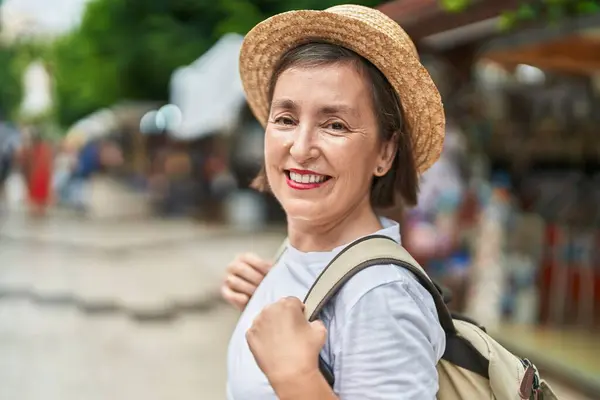 Middle age woman tourist smiling confident wearing backpack at street market