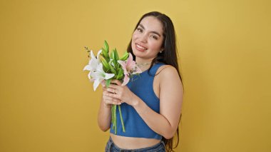 Güzel İspanyol bir kadın elinde çiçek buketiyle izole edilmiş sarı arka planda gülümsüyor.