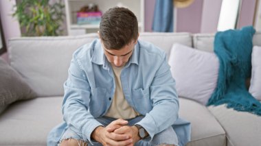 Endişeli genç İspanyol adam, oturma odasındaki kanepede oturuyor, evdeki bir sorunu düşünüyor.