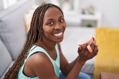 African american woman drinking coffee sitting on sofa at home