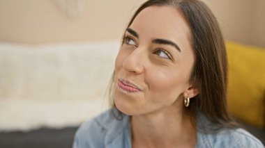 Genç, güzel, İspanyol bir kadın kanepeye oturmuş, gülümsüyor ve kendini evinde hissediyor.