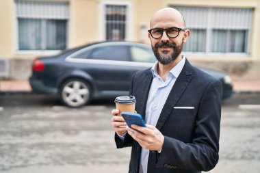Genç kel iş adamı akıllı telefon kullanıyor, sokakta kahve içiyor.