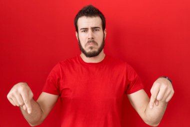 Gündelik kırmızı tişört giyen genç İspanyol adam üzgün ve üzgün görünüyor, parmaklarıyla yönü gösteriyor, mutsuz ve depresif.. 
