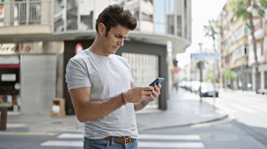Genç İspanyol adam akıllı telefon kullanıyor. Sokakta ciddi bir ifadesi var.
