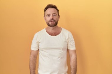 Sarı arka planda dikilen sakallı orta yaşlı adam yüzünde ciddi bir ifadeyle rahatlamış. Basit ve doğal bir şekilde kameraya bakıyorsun.. 